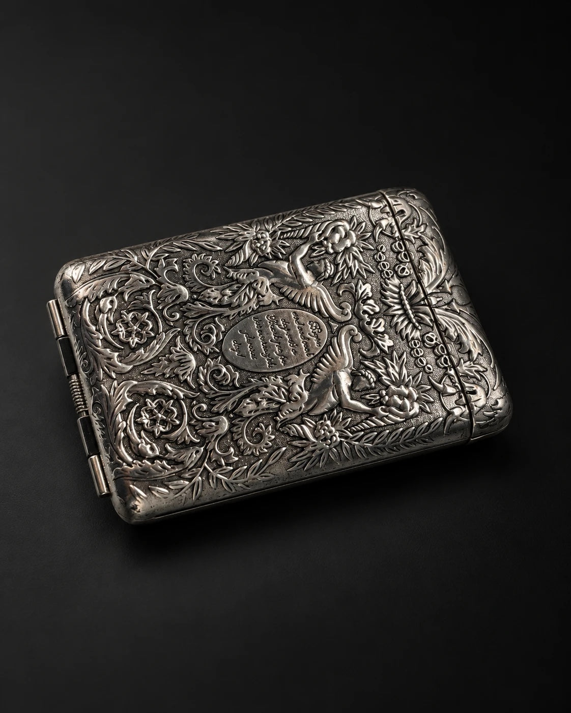 Mozane No. 1, embossed silver-tone metal case on a dark background